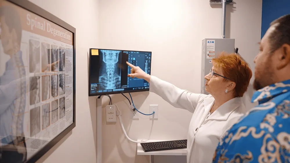 Dr. Trish Wolff pointing out findings on a spine X-ray with a patient